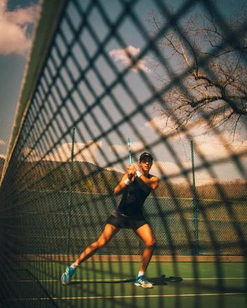 Female tennis player in action on an outdoor court, focusing on her form and technique against a scenic mountain backdrop and blue sky.