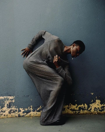 Black model in a long striped grey dress bending backwards against a dark blue textured wall in Paris.