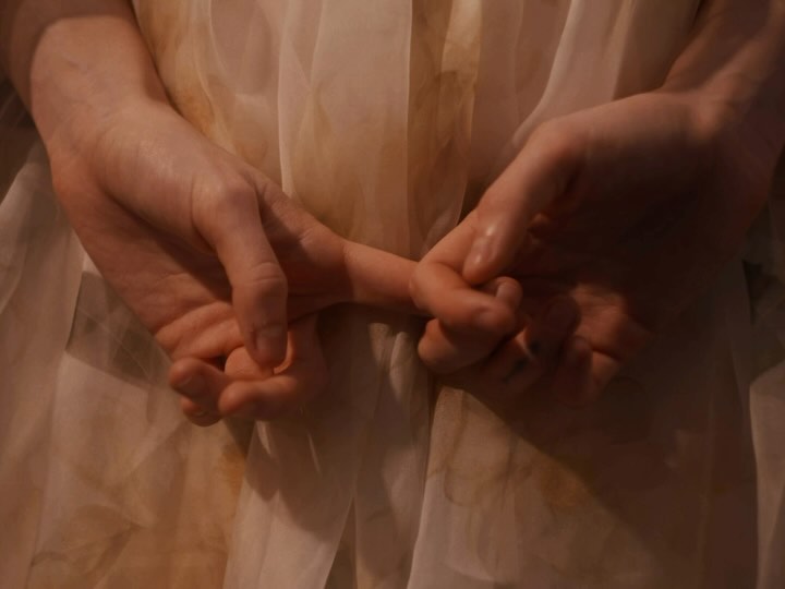 Close-up of adult and child hands intertwined against a soft-focus, light-colored fabric background, evoking a tender family moment.