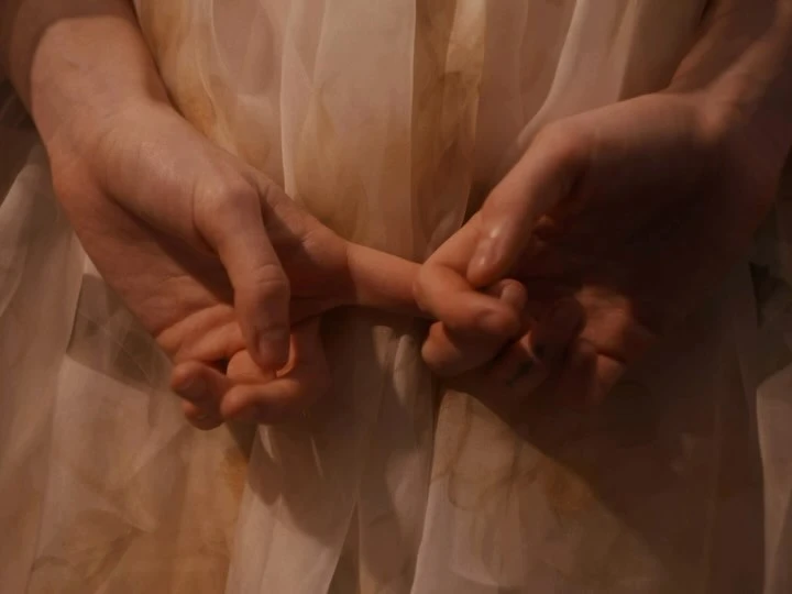 Close-up of adult and child hands intertwined against a soft-focus, light-colored fabric background, evoking a tender family moment.