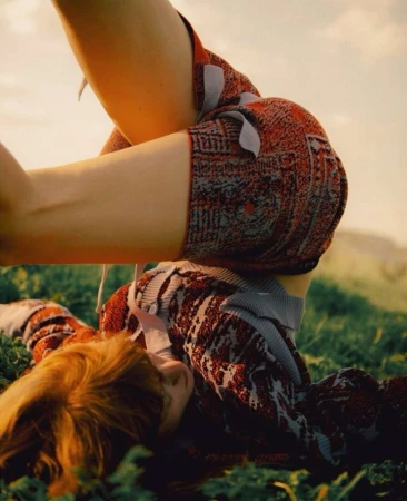 Model lying upside down in a grassy meadow wearing patterned red knit shorts and a matching button-up cardigan by Noemi Ottilia Szabo