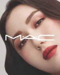 Close-up beauty portrait of an East Asian woman wearing warm coral eyeshadow and bold red lipstick with a white MAC logo overlay.