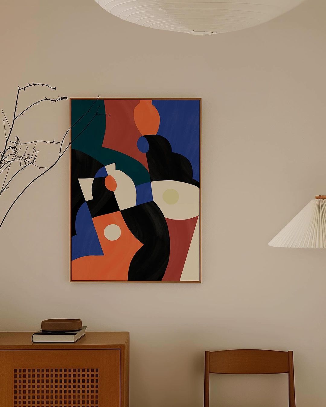Abstract geometric painting in blue, orange, and black, hanging on a neutral wall above a wooden cabinet in a naturally lit interior.