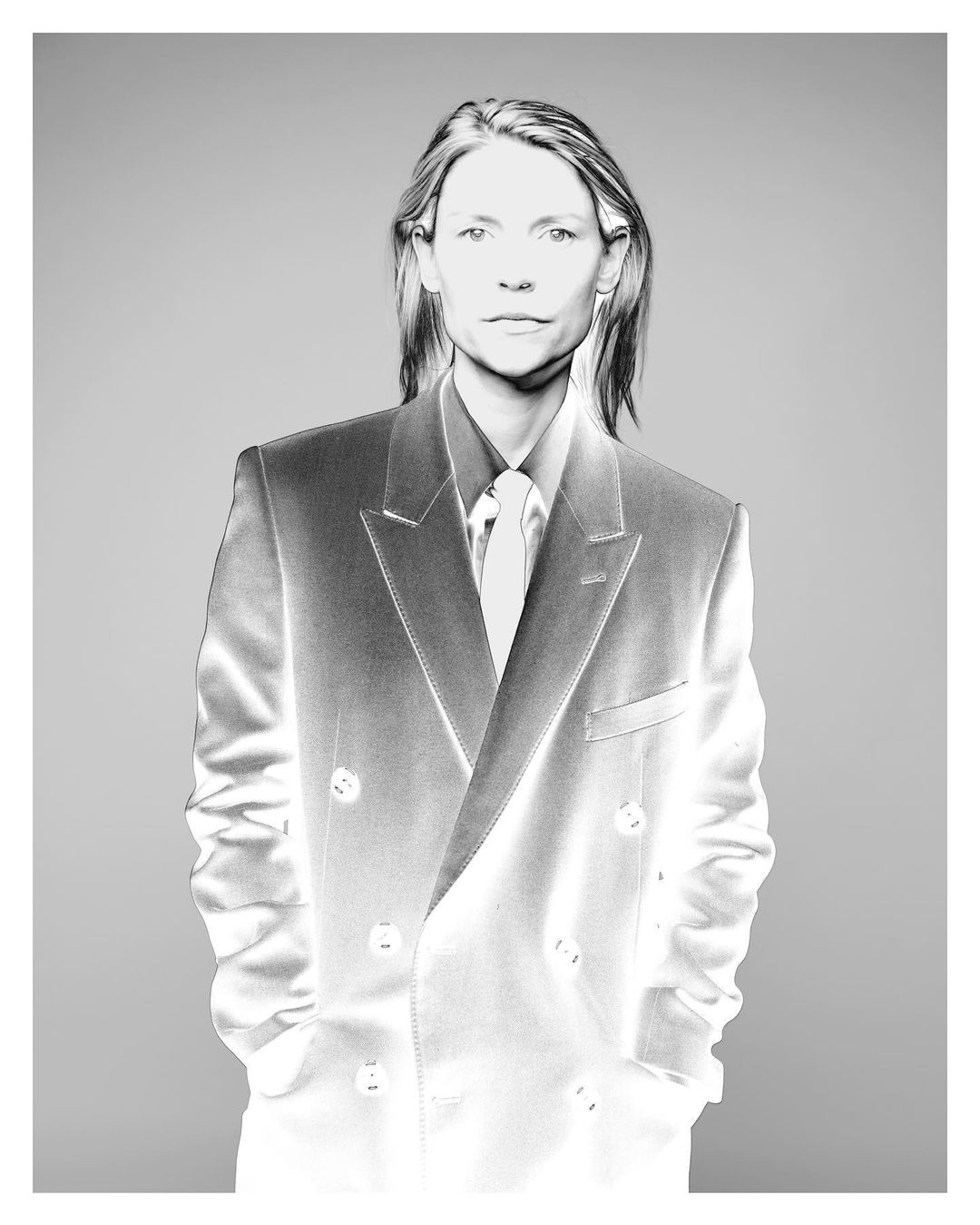 Monochromatic portrait of a woman in a business suit, tie, and collared shirt standing in a neutral indoor setting.