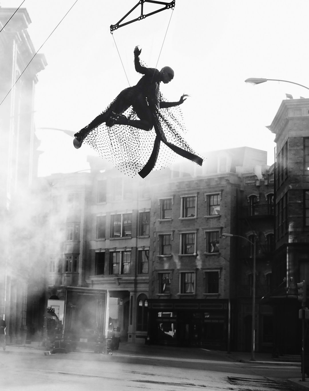 A black-and-white photo of a floating human figure suspended above a city street amid a misty atmosphere, creating a surreal effect.