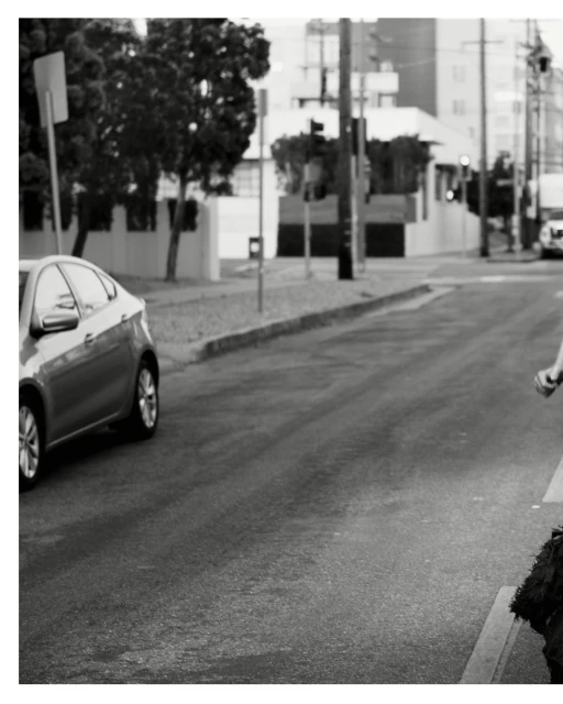 Black and white shot of a car on a road next to a curb, with a glimpse of a person on the right side of the frame.