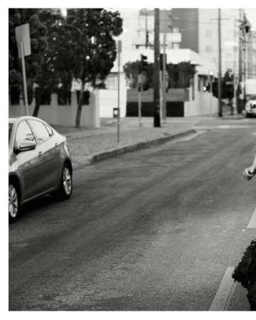 Black and white shot of a car on a road next to a curb, with a glimpse of a person on the right side of the frame.