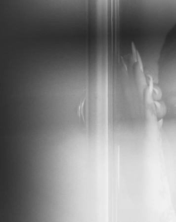 Close-up of a person's hand with long nails gripping a metal bar; the image is black and white with a soft, blurred effect.
