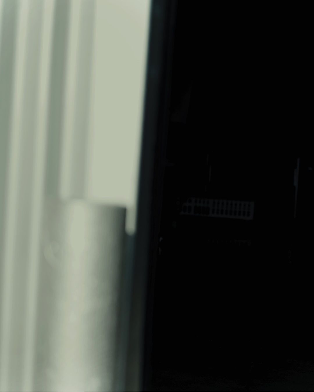 Close-up of a modern black refrigerator with white curtains visible in the background, suggesting a clean and minimalist interior design.