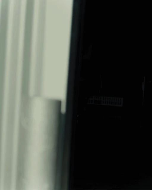 Close-up of a modern black refrigerator with white curtains visible in the background, suggesting a clean and minimalist interior design.