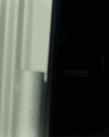 Close-up of a modern black refrigerator with white curtains visible in the background, suggesting a clean and minimalist interior design.