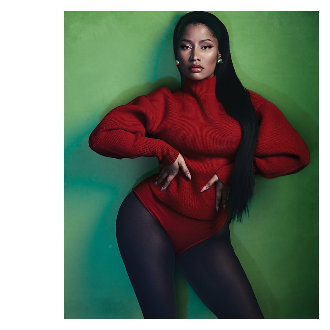 Portrait of a woman with long black hair wearing a red long-sleeve top and dark tights posing against a vibrant green backdrop.