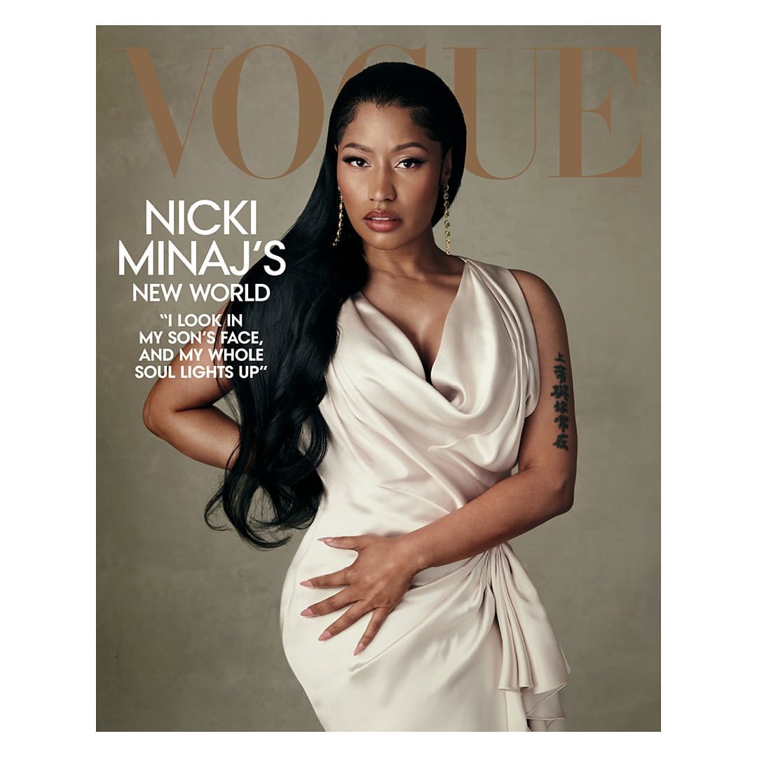 Nicki Minaj graces the cover of Vogue, posing in a draped gown with long black hair and statement earrings against a neutral backdrop.