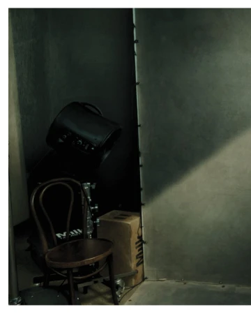 Behind-the-scenes shot of a wooden chair and studio equipment in a dim room by photographer Norman Jean Roy