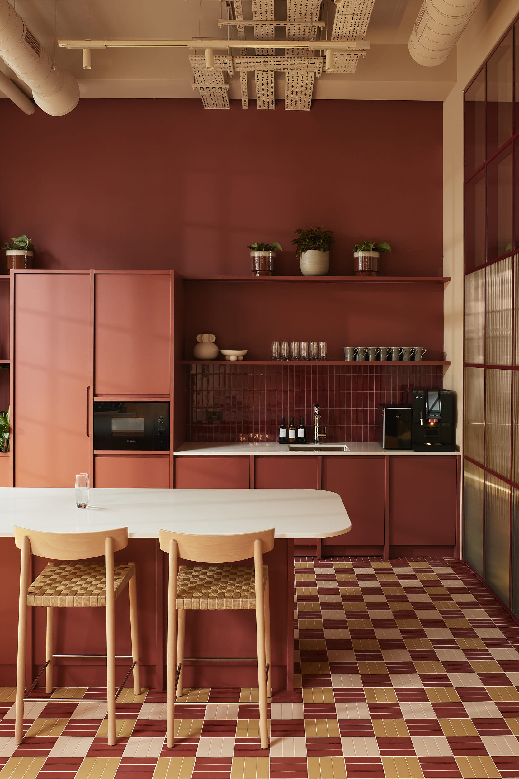 Modern kitchen interior featuring terracotta cabinetry, an island with two wooden barstools, and a checkered tiled floor.