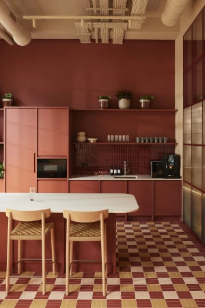 Modern kitchen interior featuring terracotta cabinetry, an island with two wooden barstools, and a checkered tiled floor.