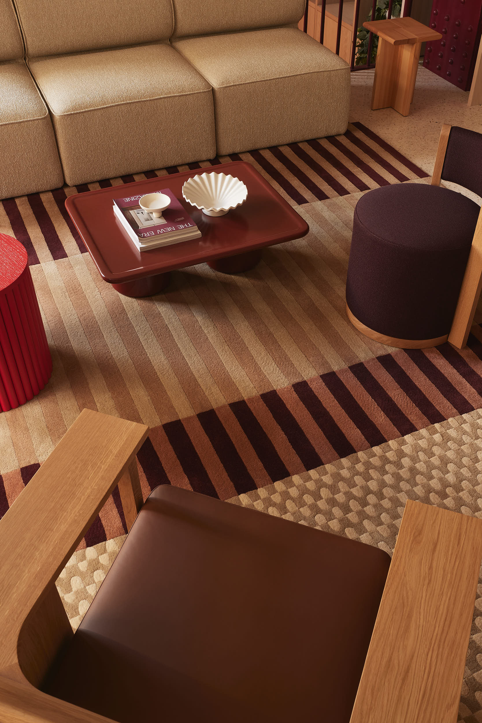 High-angle view of a modern living room interior with a beige sectional sofa, striped area rugs, and a low red coffee table.