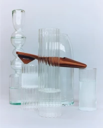 Copper Prada shoe resting horizontally atop vertical transparent glass vases against a pale background