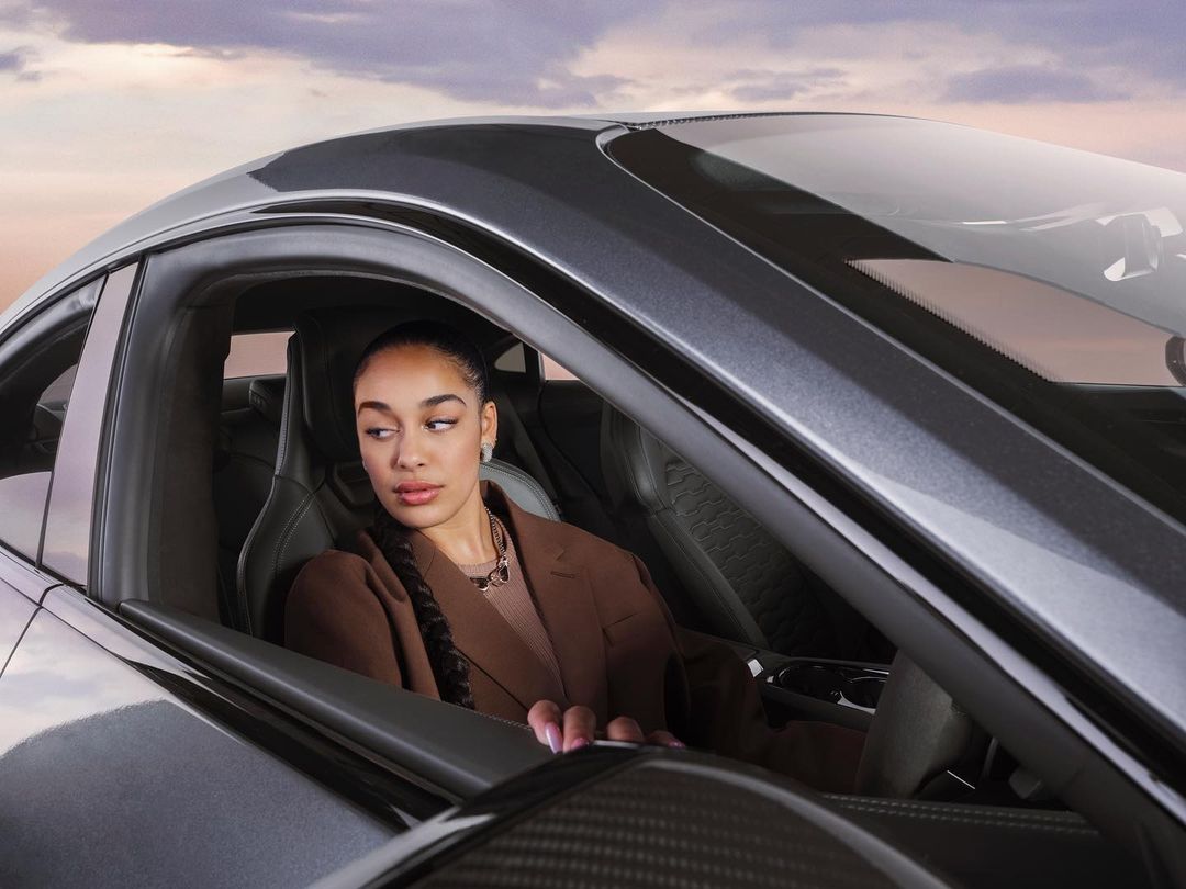 Woman inside a gray sports car in a medium shot with a dramatic sky background, showcasing automotive and beauty elements.
