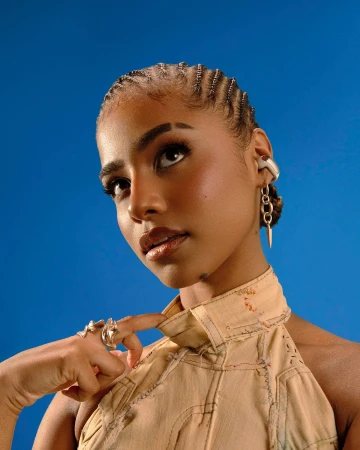 Portrait of a Black woman with cornrows and sculpted rings against a solid blue background by photographer Nwaka Okparaeke.