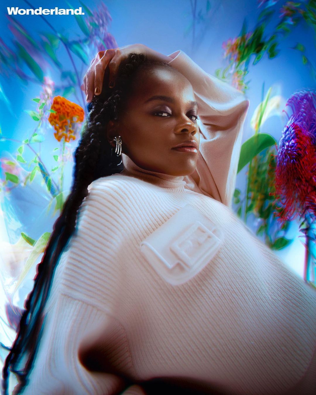 Portrait of woman with braided hair wearing a turtleneck sweater and posing in a floral background with cool-toned, blurred bokeh.