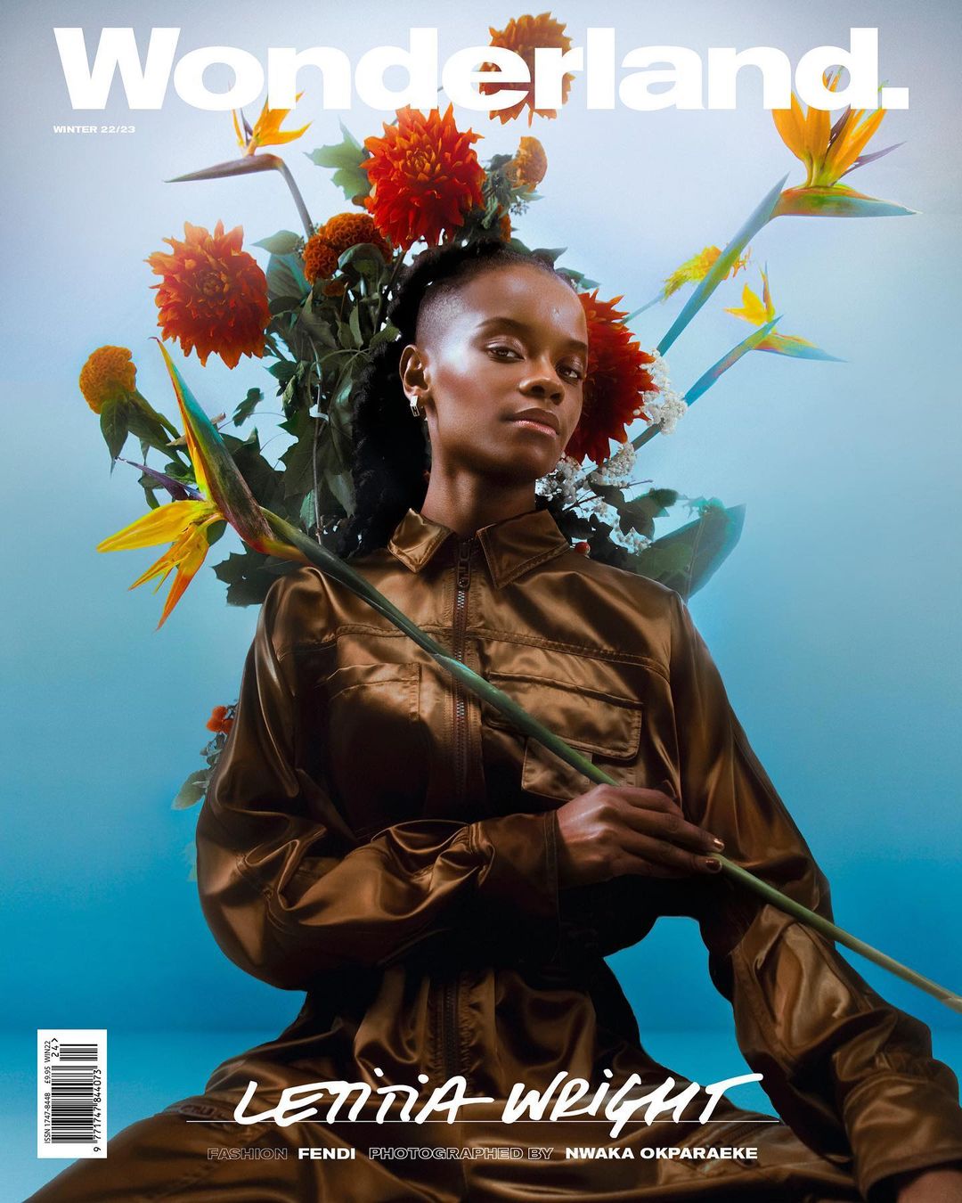 Magazine cover features Letitia Wright wearing a brown jumpsuit surrounded by orange dahlias and bird of paradise flowers against light blue.