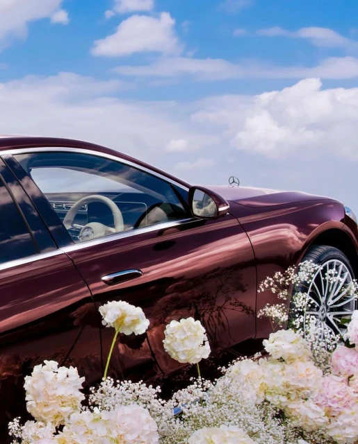 Burgundy luxury car exterior with white floral arrangement against a blue sky. Automotive elegance meets nature's beauty in a captivating scene.