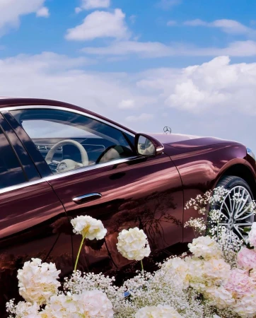 Burgundy luxury car exterior with white floral arrangement against a blue sky. Automotive elegance meets nature's beauty in a captivating scene.