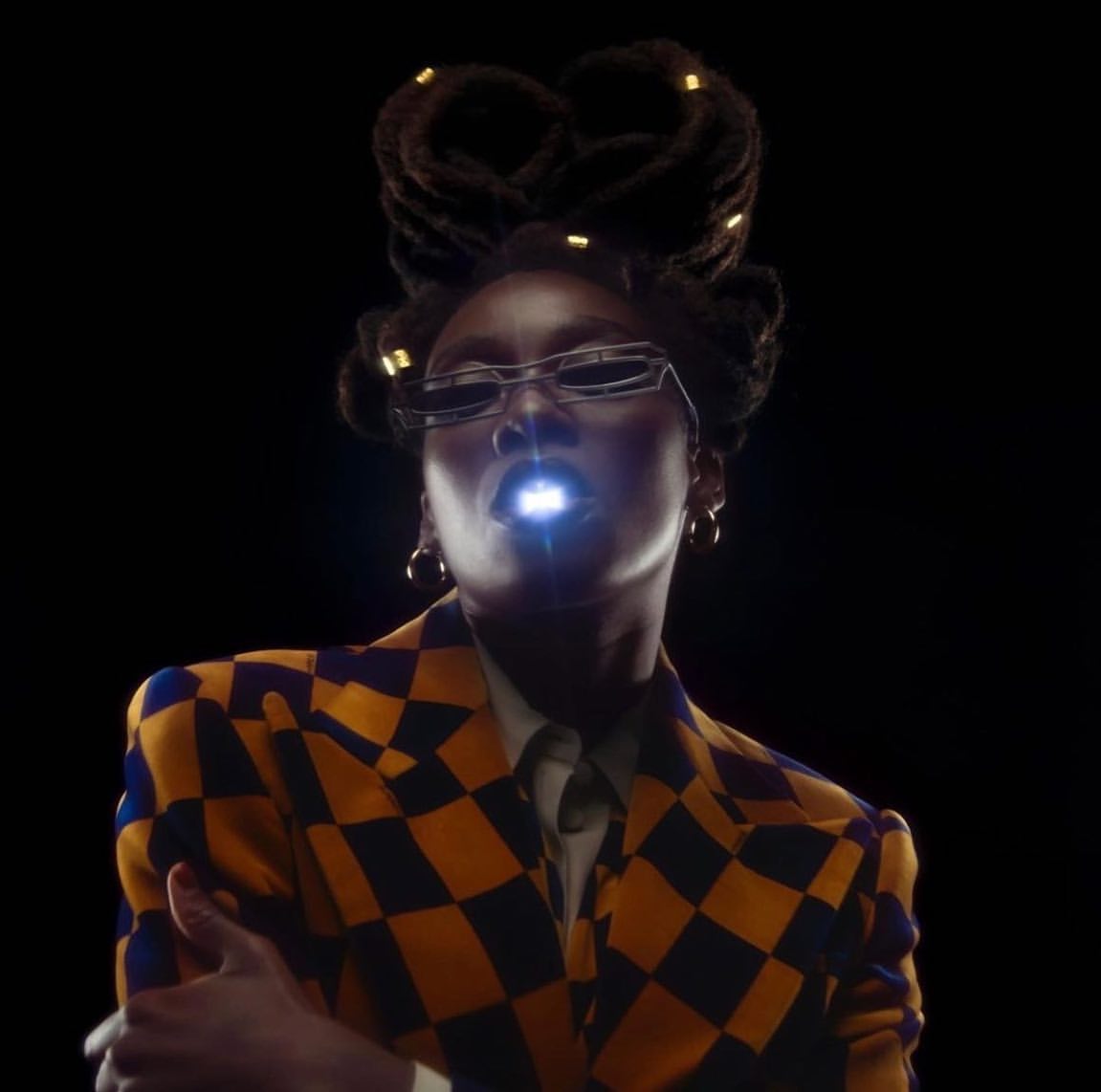 Stylish African woman in a checkered jacket poses against a dark background, illuminated by a bright light emanating from her mouth.