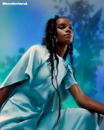 Black woman wearing a light blue dress kneeling against a blurred blue and green gradient backdrop by photographer Nwaka Okparaeke
