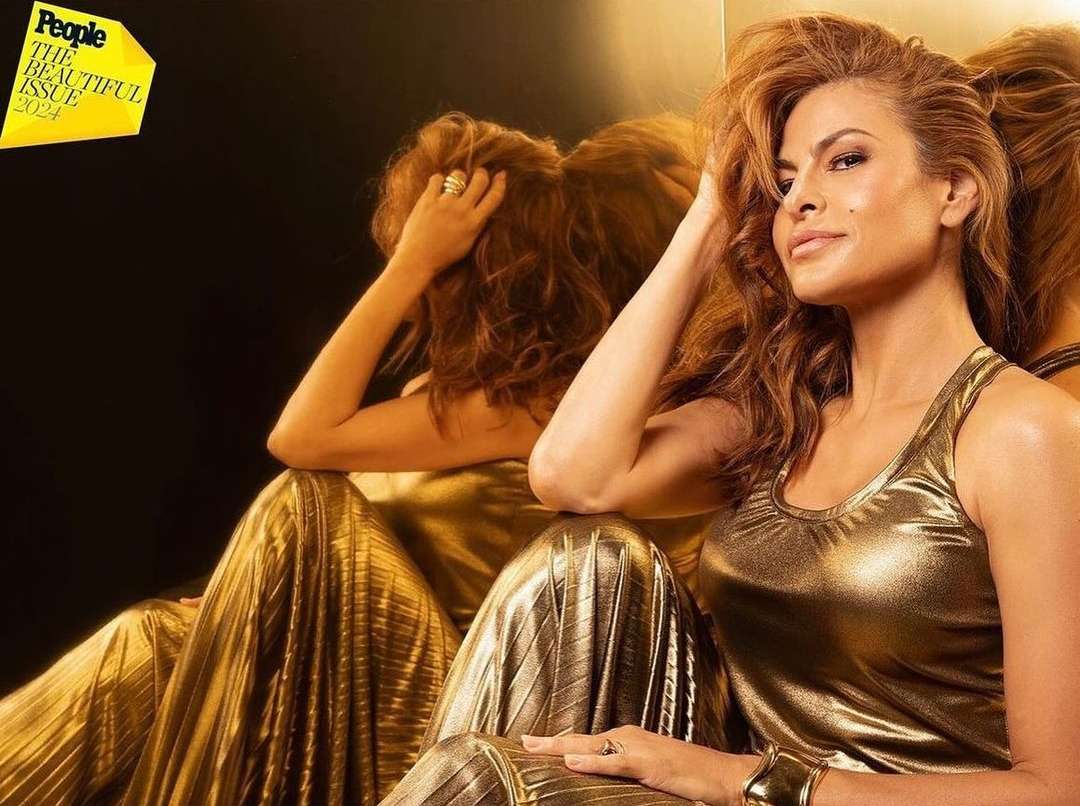 Eva Mendes poses in a gold dress for People Magazine's The Beautiful Issue 2024, reflected in a mirror with a dark background.