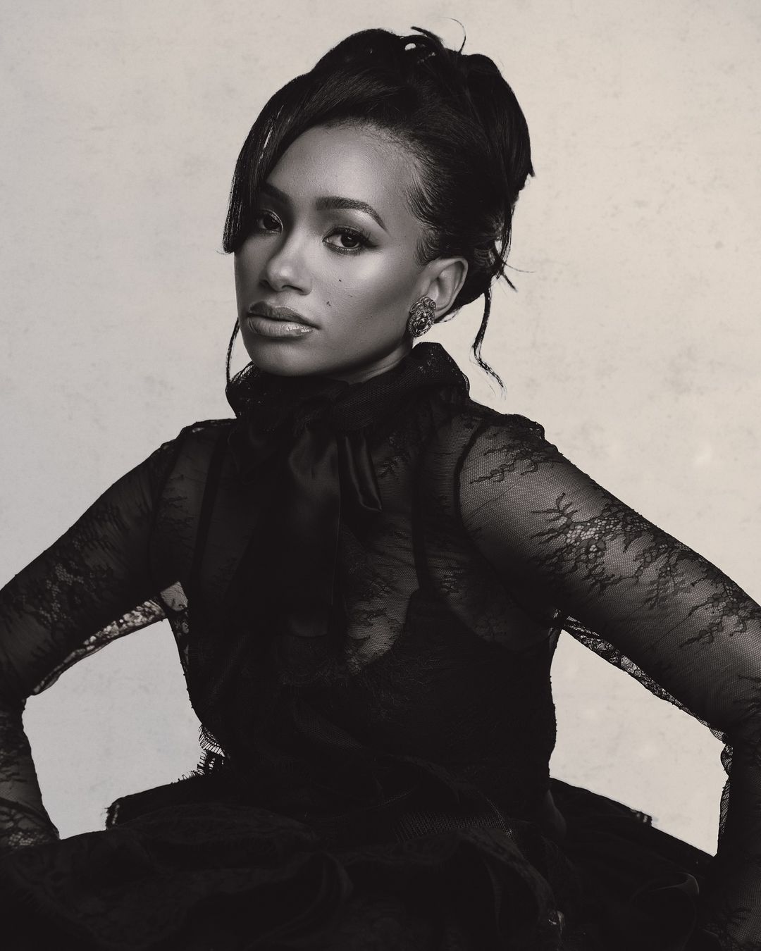 Monochromatic portrait of a Black adult woman with updo, wearing lace top with high collar, looking at the camera against a light background.