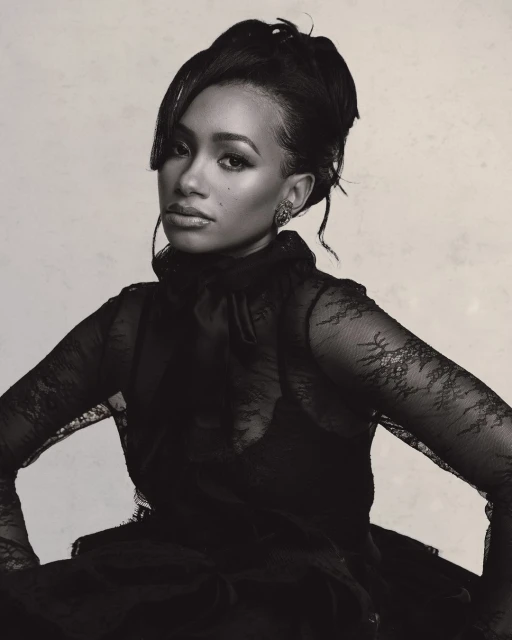 Monochromatic portrait of a Black adult woman with updo, wearing lace top with high collar, looking at the camera against a light background.