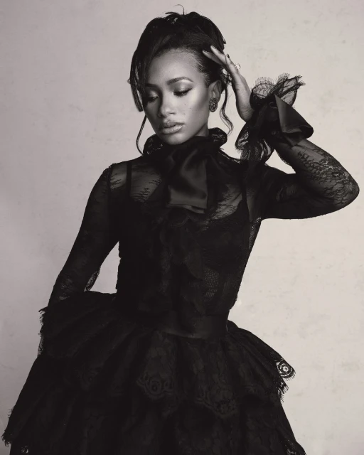 Monochrome portrait of a woman wearing a black lace dress with a high neckline and ruffled sleeves, posing in front of a neutral backdrop.