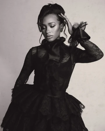 Monochrome portrait of a woman wearing a black lace dress with a high neckline and ruffled sleeves, posing in front of a neutral backdrop.