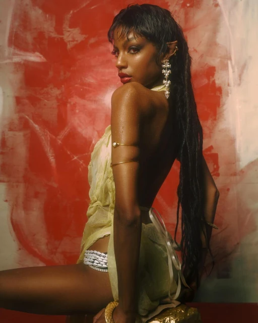 A dark-skinned woman with pointed ears, back turned to the camera, poses in a yellow dress against a red and white abstract backdrop.