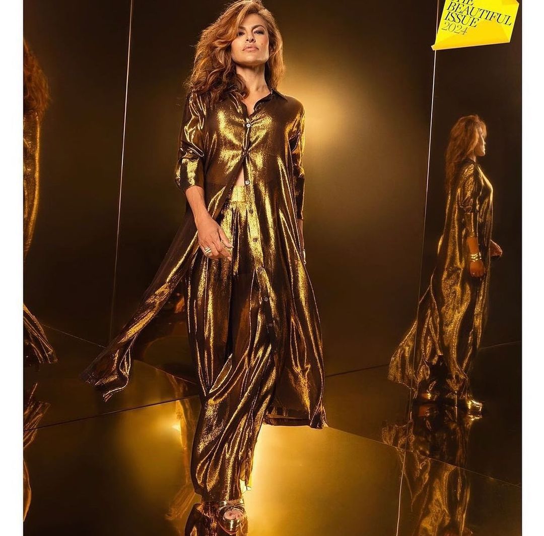 Eva Mendes in golden outfit poses in front of a reflective gold background for a magazine cover, showcasing fashion and celebrity.