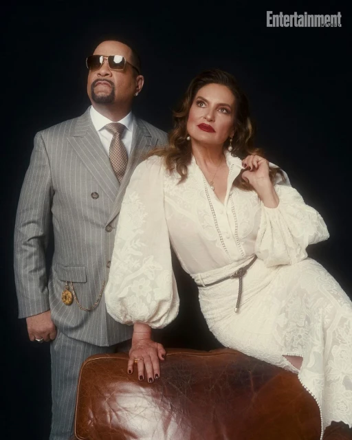 Portrait of Ice-T in a grey suit and Coco Austin in a white lace dress, posed against a dark backdrop with a leather trunk.