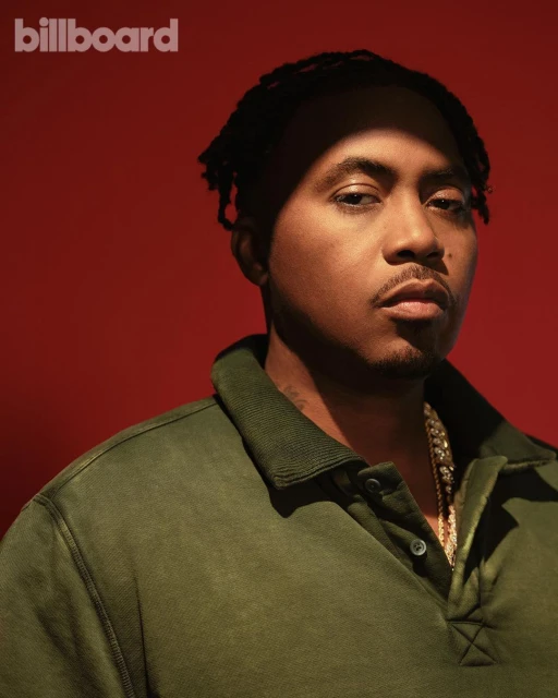 Portrait of the American rapper Nas in an olive green polo shirt with a gold chain necklace against a solid red background.