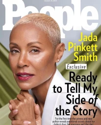 Close-up portrait of Jada Pinkett Smith with short bleached blonde hair and white top against a soft green background.