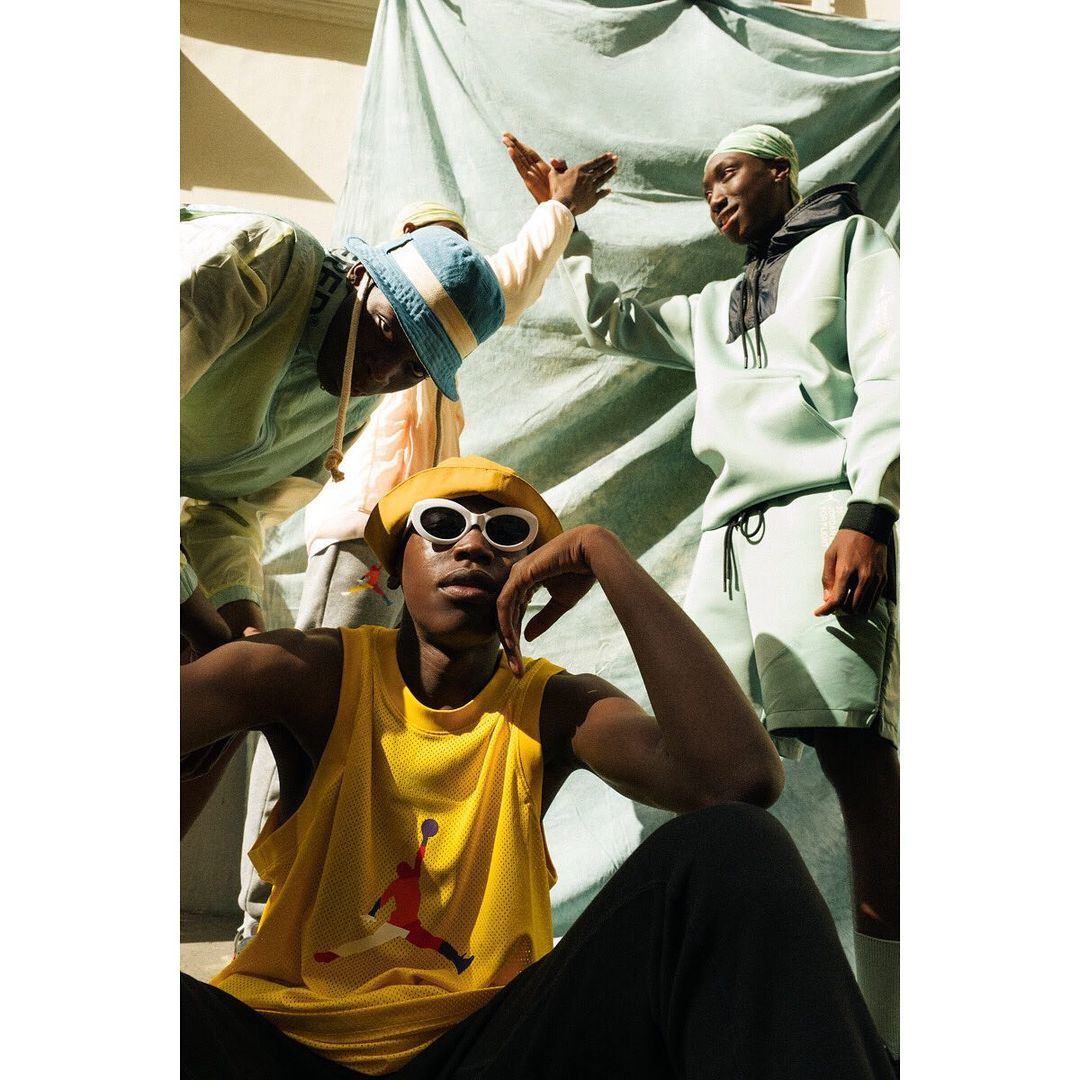 Three young Black adults wearing streetwear fashion in an outdoor setting, posing in casual wear with a blue and turquoise backdrop.