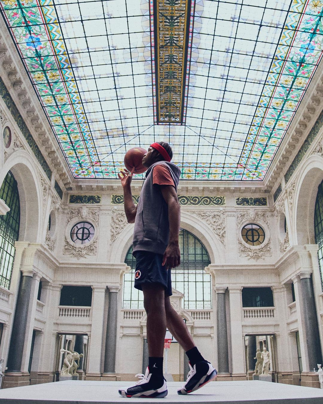 An adult male balances a basketball on his finger in a light and airy museum setting, showcasing a unique blend of sport and architecture.