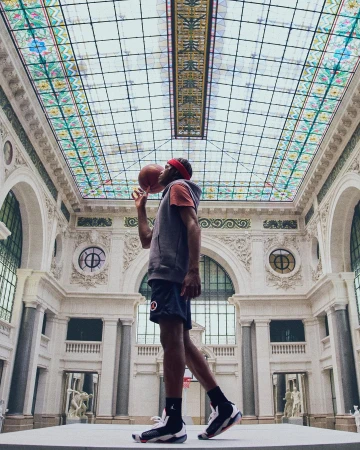 An adult male balances a basketball on his finger in a light and airy museum setting, showcasing a unique blend of sport and architecture.