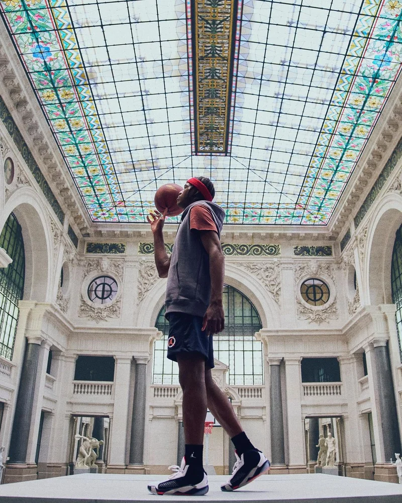 A basketball player spinning a ball on his finger inside a grand historic hall with an ornate glass ceiling, photographed by Ojoz.