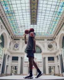 A basketball player spinning a ball on his finger inside a grand historic hall with an ornate glass ceiling, photographed by Ojoz.