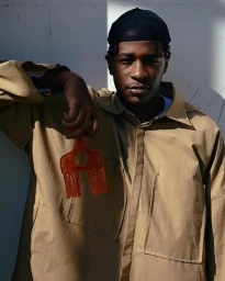 Portrait of a Black man wearing a tan collared shirt and black durag, holding an amber hair pick in Paris by Ojoz.