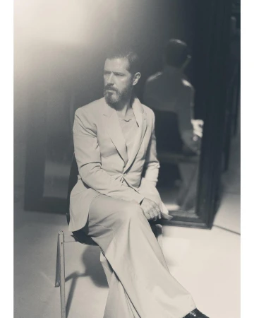Monochrome portrait of a bearded man in a tailored suit seated on a chair, reflected in a mirror behind him in Paris by Ola Rindal.
