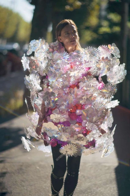 Woman in shimmering floral dress walks outdoors on sunny day. Iridescent pastel colors. Fashion editorial look. Unusual clothing.