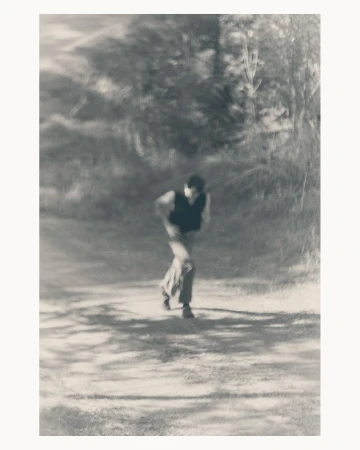 Motion blurred black and white photograph of a man running along a sunlit pathway framed by trees, captured by Ola Rindal.