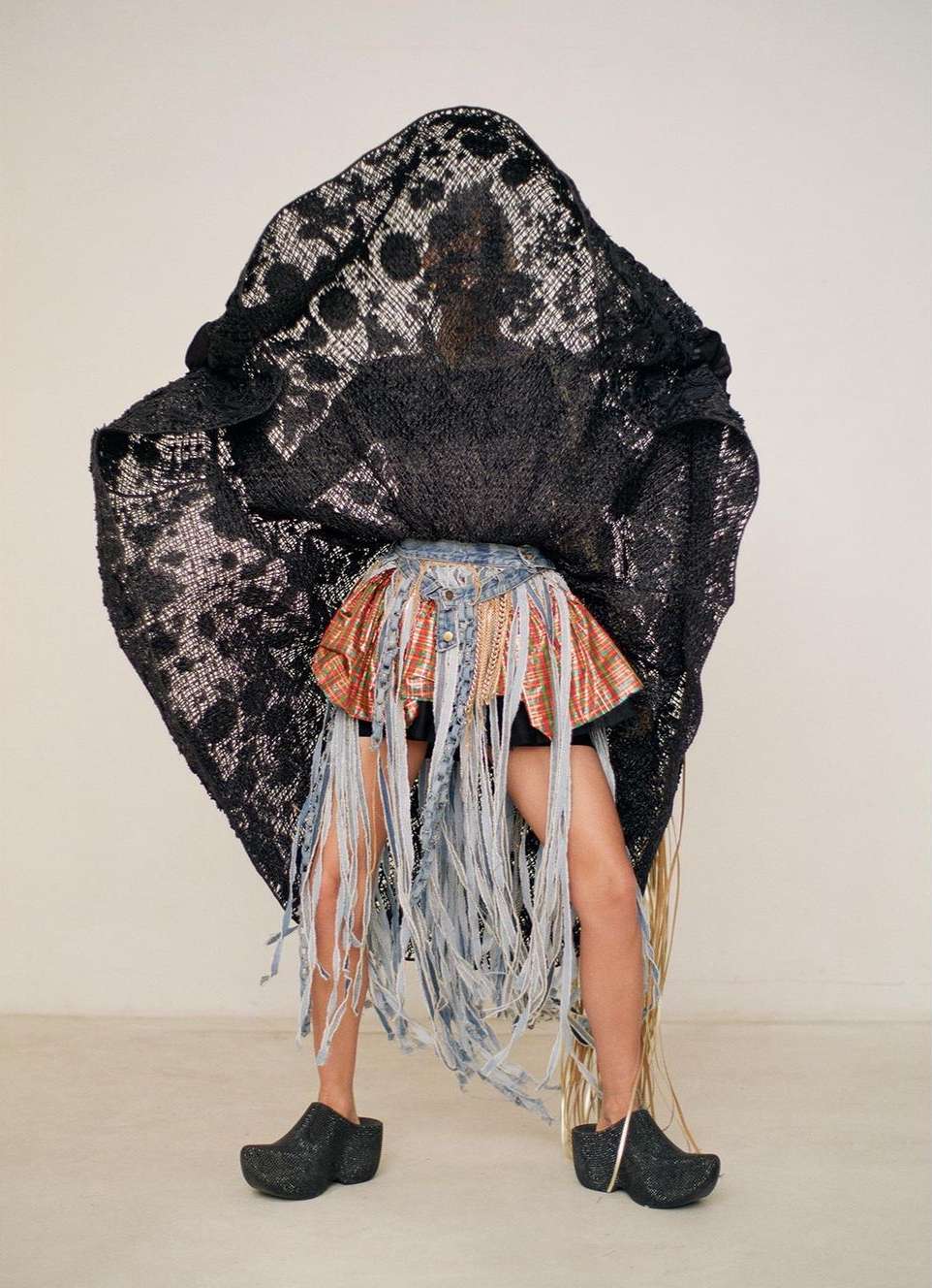 Person wearing an elaborate skirt and lace covering posing in front of a white wall inside a photo studio, studio lighting.